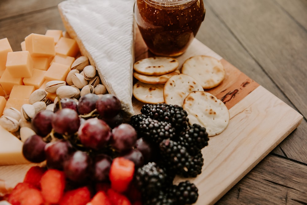 a wooden cutting board topped with cheese, fruit and crackers