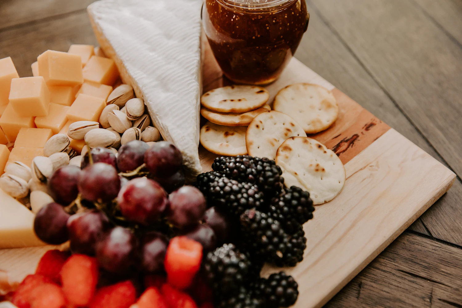 A board of cheese, oatcakes and grapes beside an open jar of amber preserve