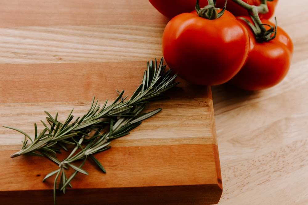 a wooden cutting board topped with tomatoes and a sprig of rosemary