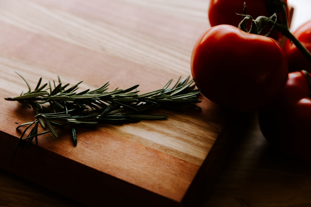 a wooden cutting board topped with tomatoes and a sprig of rosemary