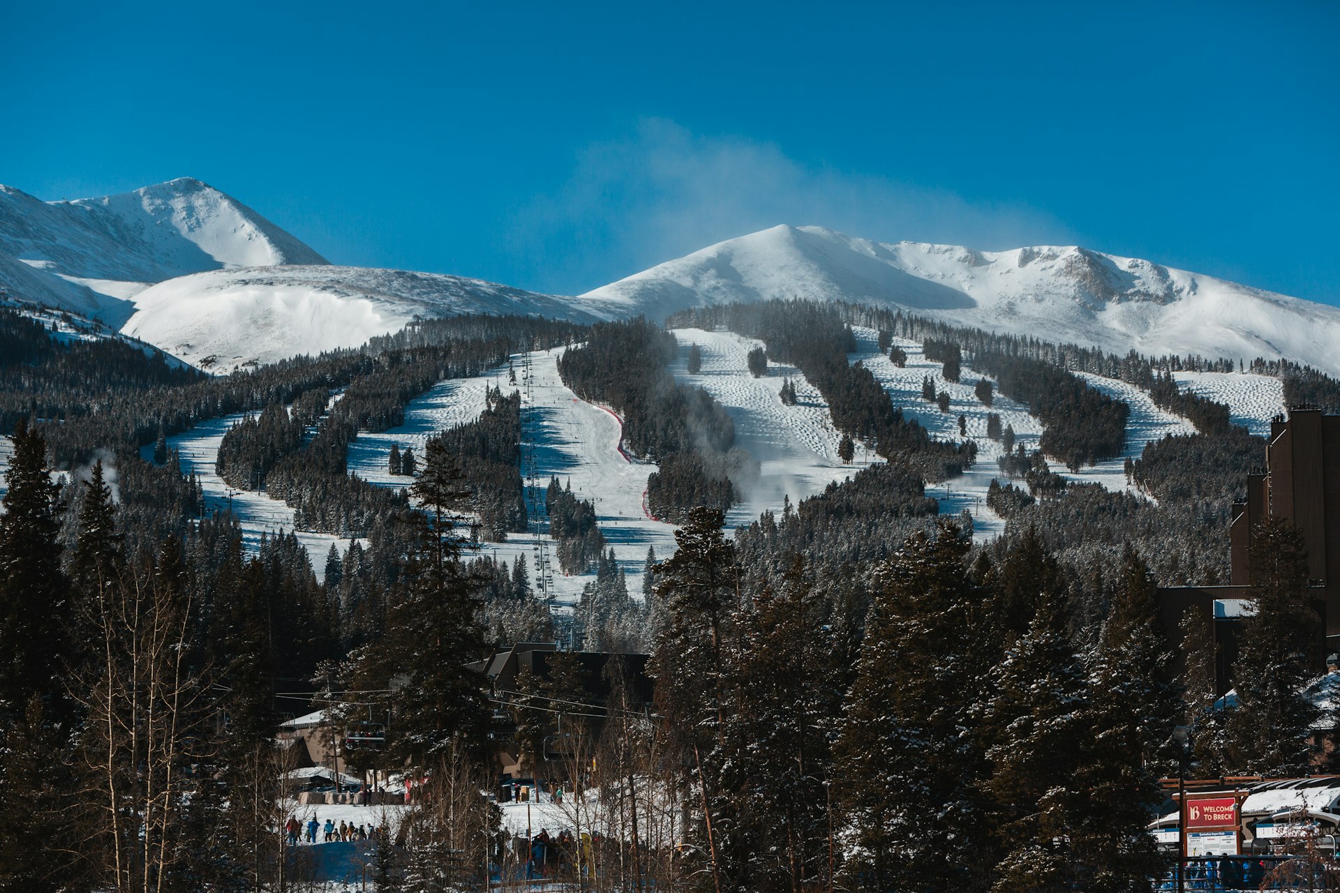 Ski runs cut through pine forest below snowy peaks at a Colorado resort
