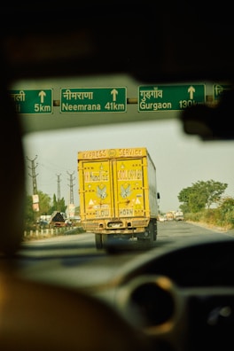 a yellow truck driving down a street next to a green sign