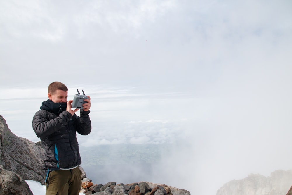 ein Mann, der auf dem Gipfel eines Berges steht und eine Kamera hält
