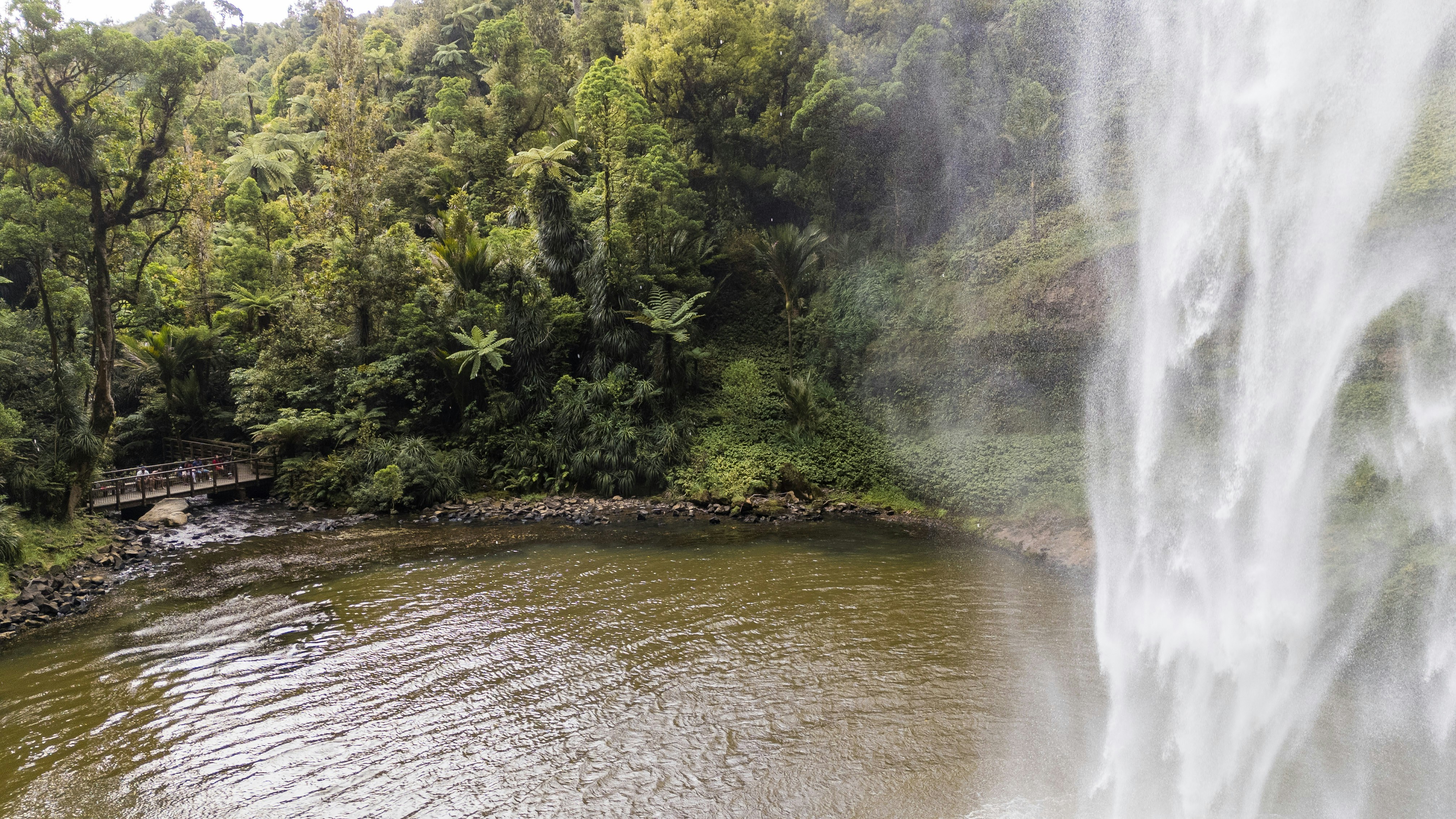 a large waterfall with a bridge over a body of water, 