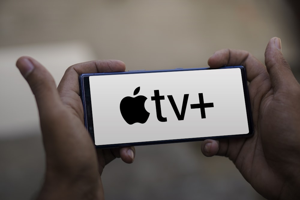 a person holding a smart phone with the apple tv plus logo on it