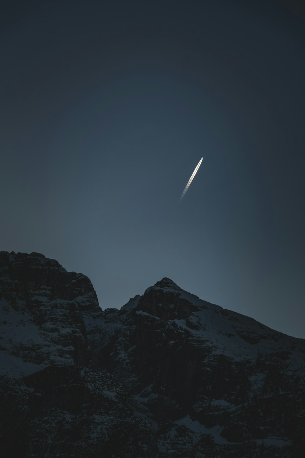 a jet flying over a mountain under a dark sky
