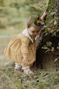 a little girl standing next to a tree
