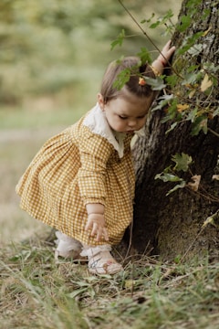 a little girl standing next to a tree