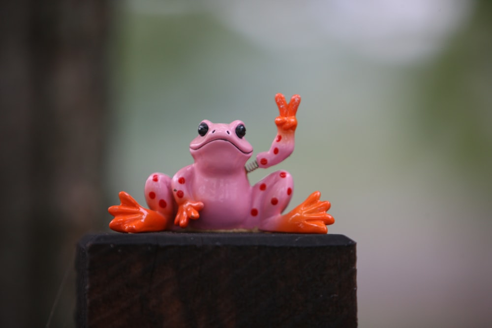 a pink frog sitting on top of a wooden block