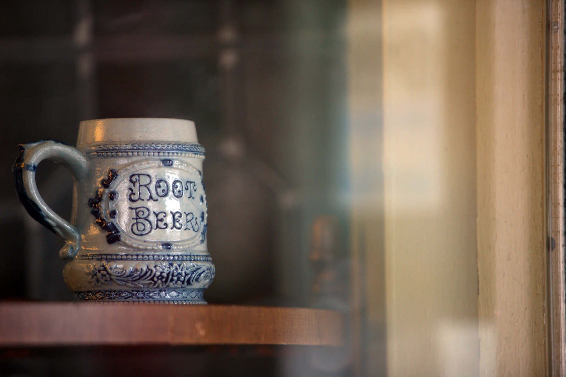 A gray salt-glazed stoneware mug with cobalt blue decoration standing on a wooden shelf behind glass