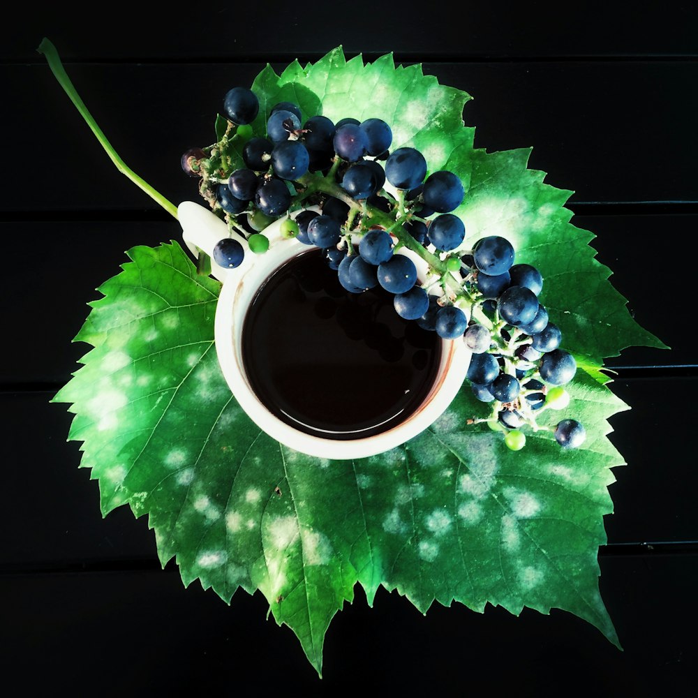 a cup of coffee and some grapes on a leaf