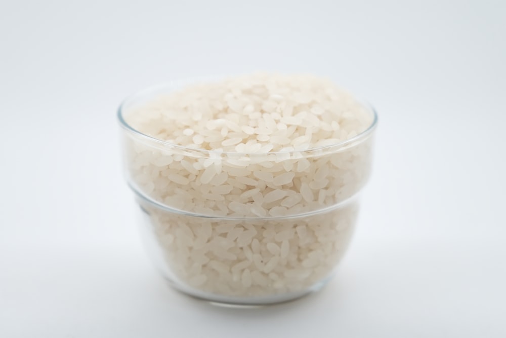 uma tigela de vidro cheia de arroz em cima de uma mesa branca