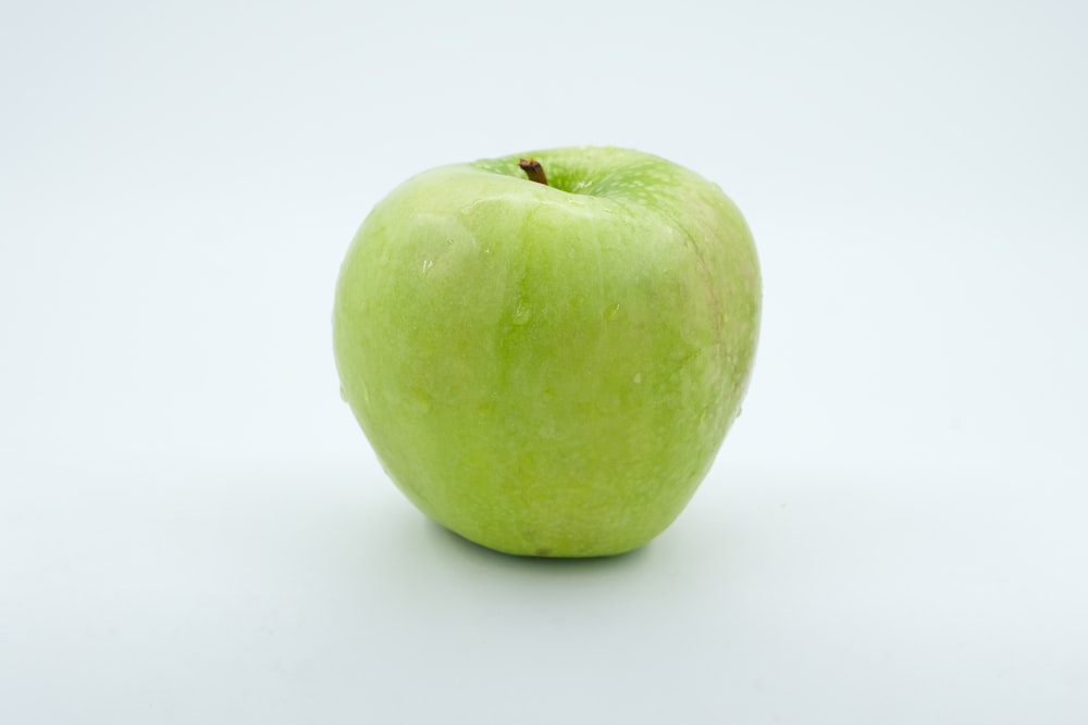 a green apple sitting on top of a white table