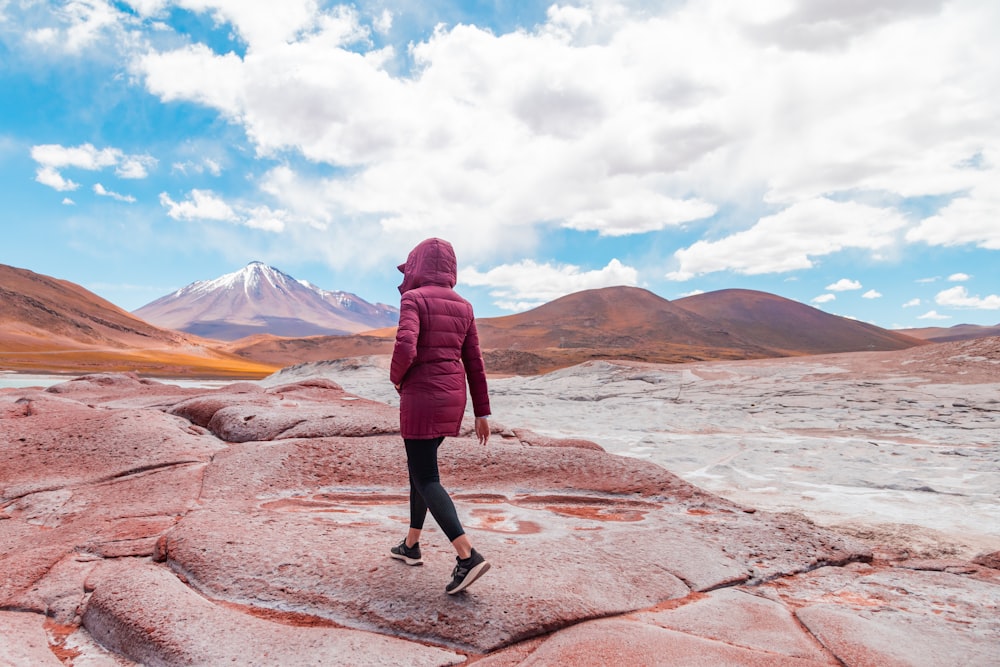 a woman in a red jacket is walking on a rock