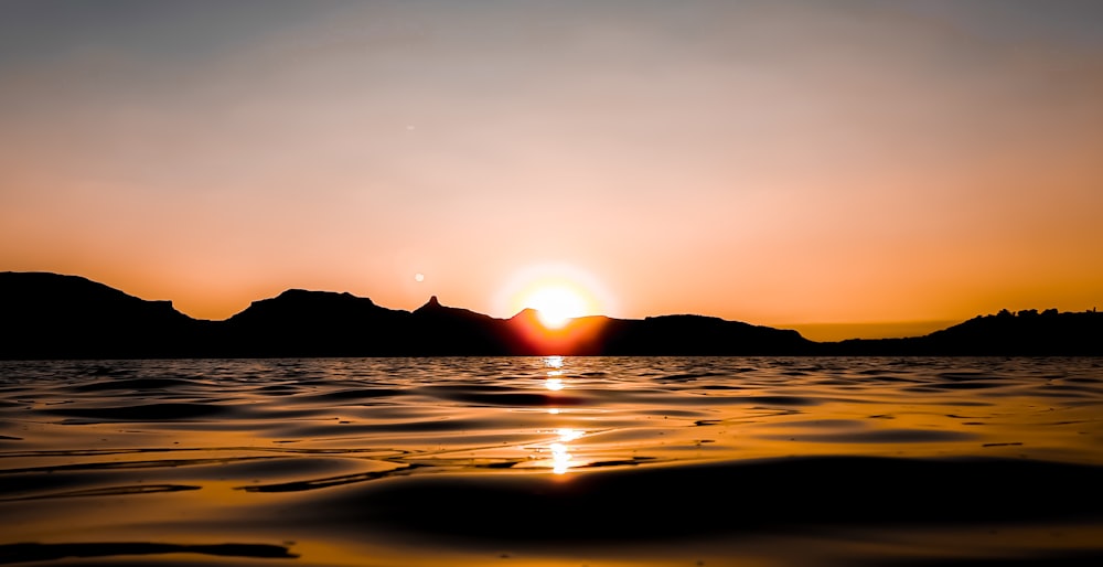 the sun is setting over the water with mountains in the background