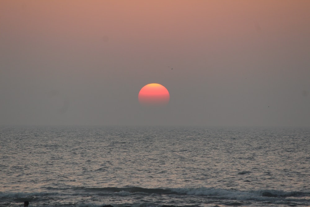 the sun is setting over the ocean on a hazy day