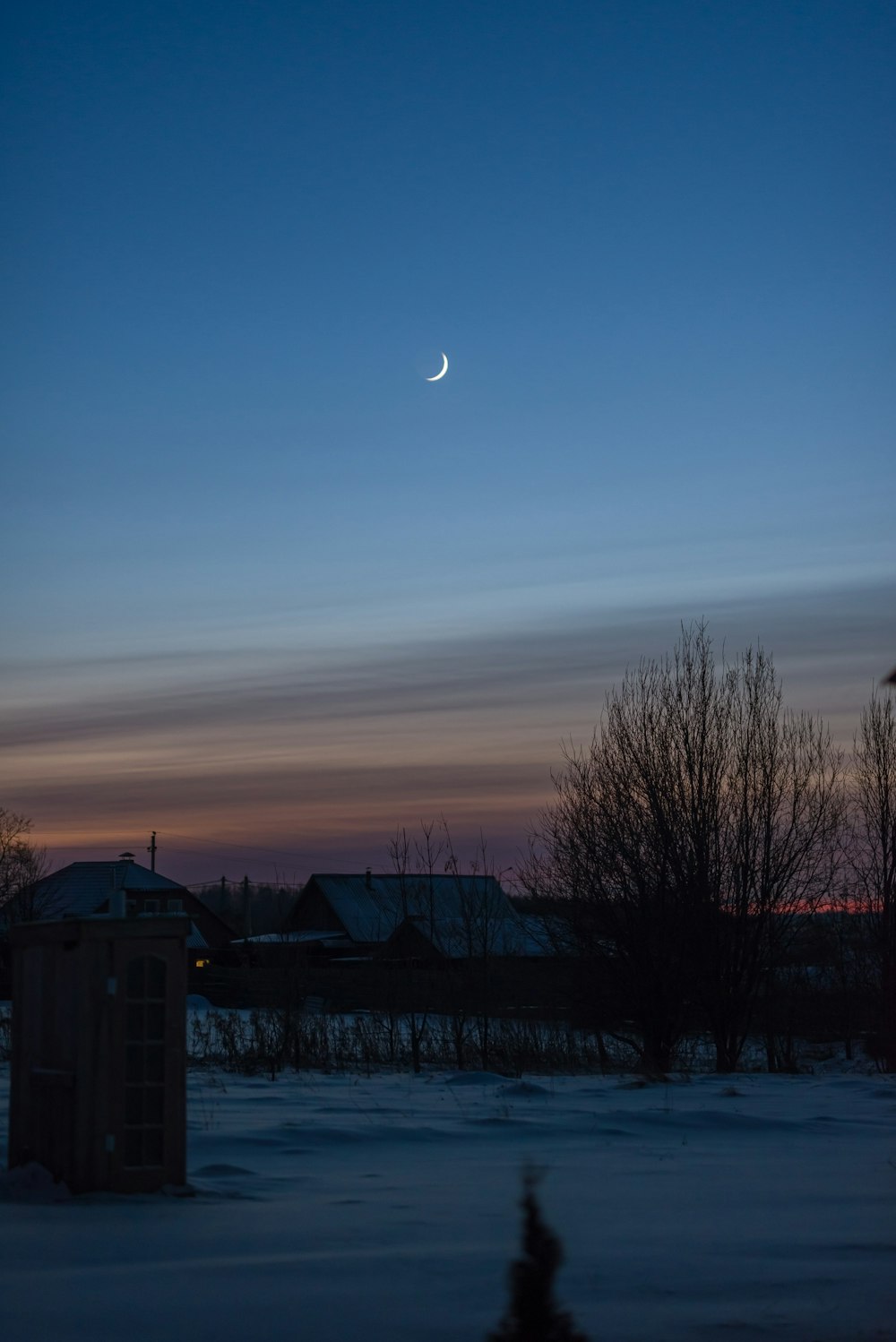 the moon is seen in the sky over a snow covered field