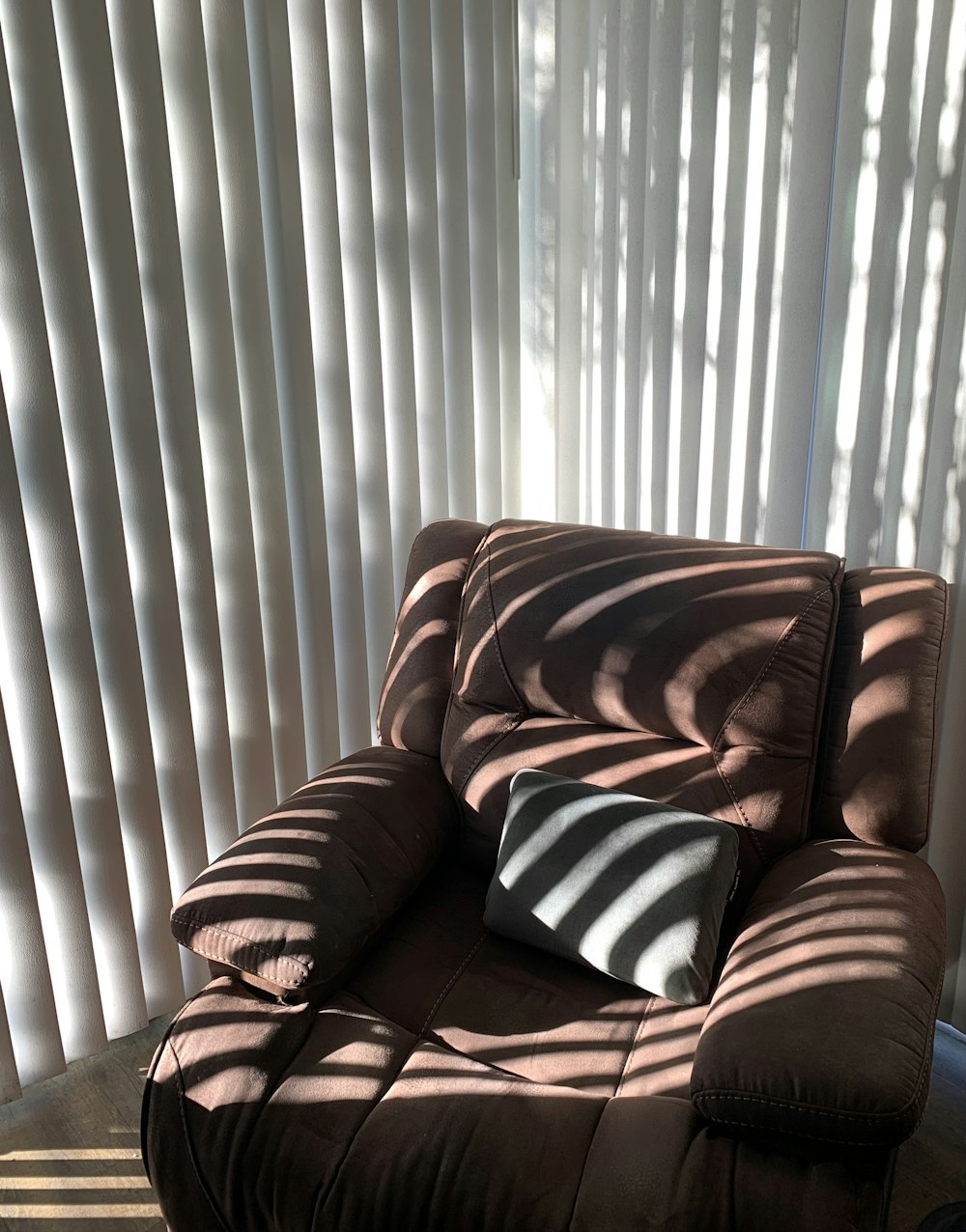 a brown chair sitting in front of a window covered in blinds