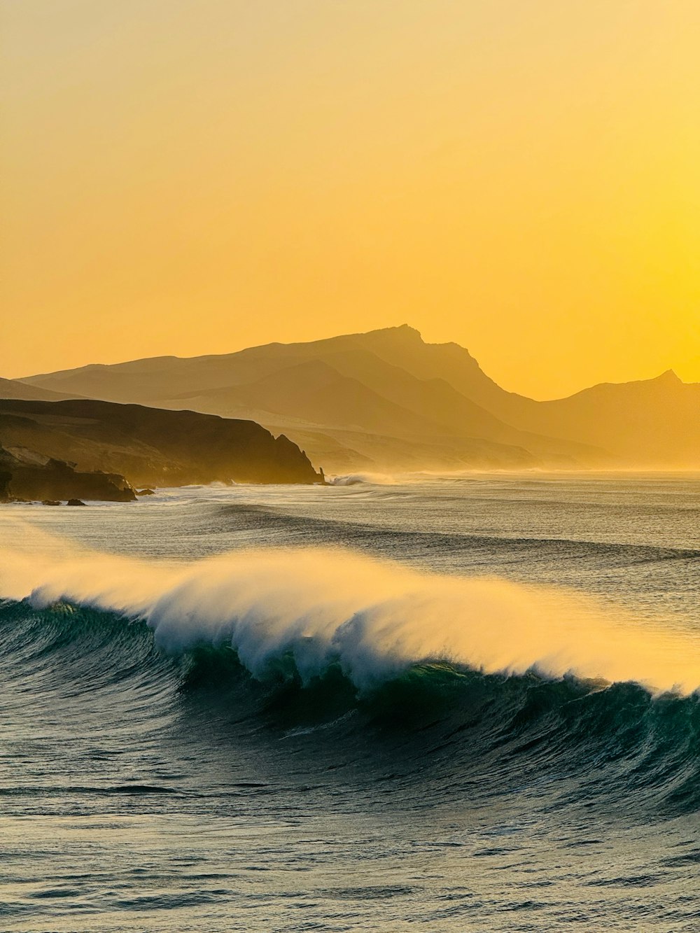 a large wave in the ocean with mountains in the background