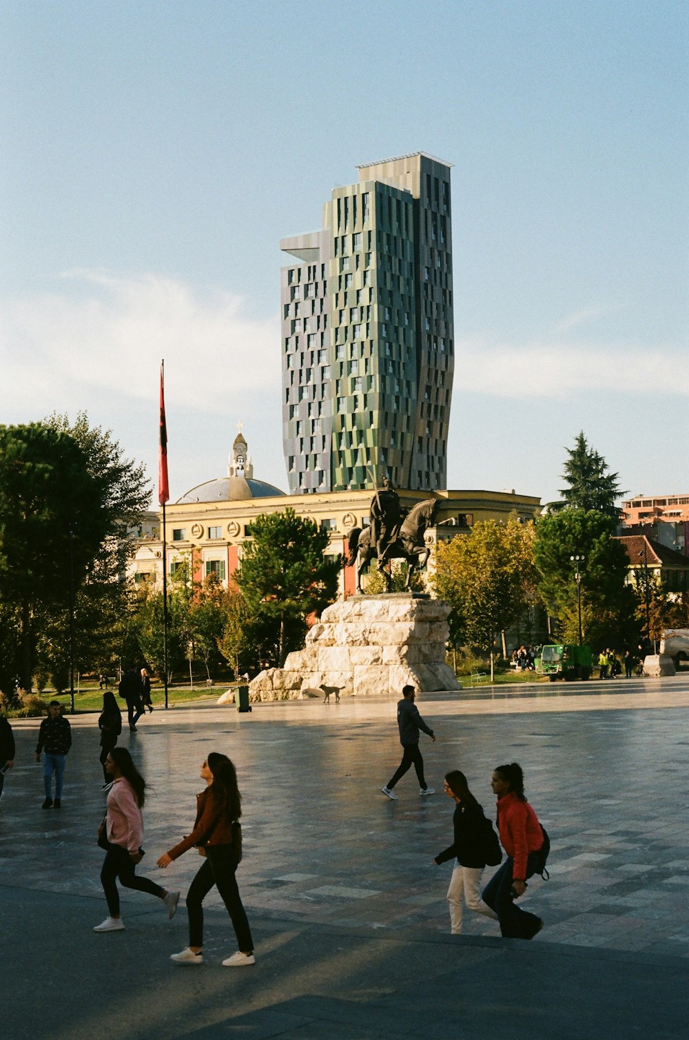 a group of people walking across a parking lot next to a tall building