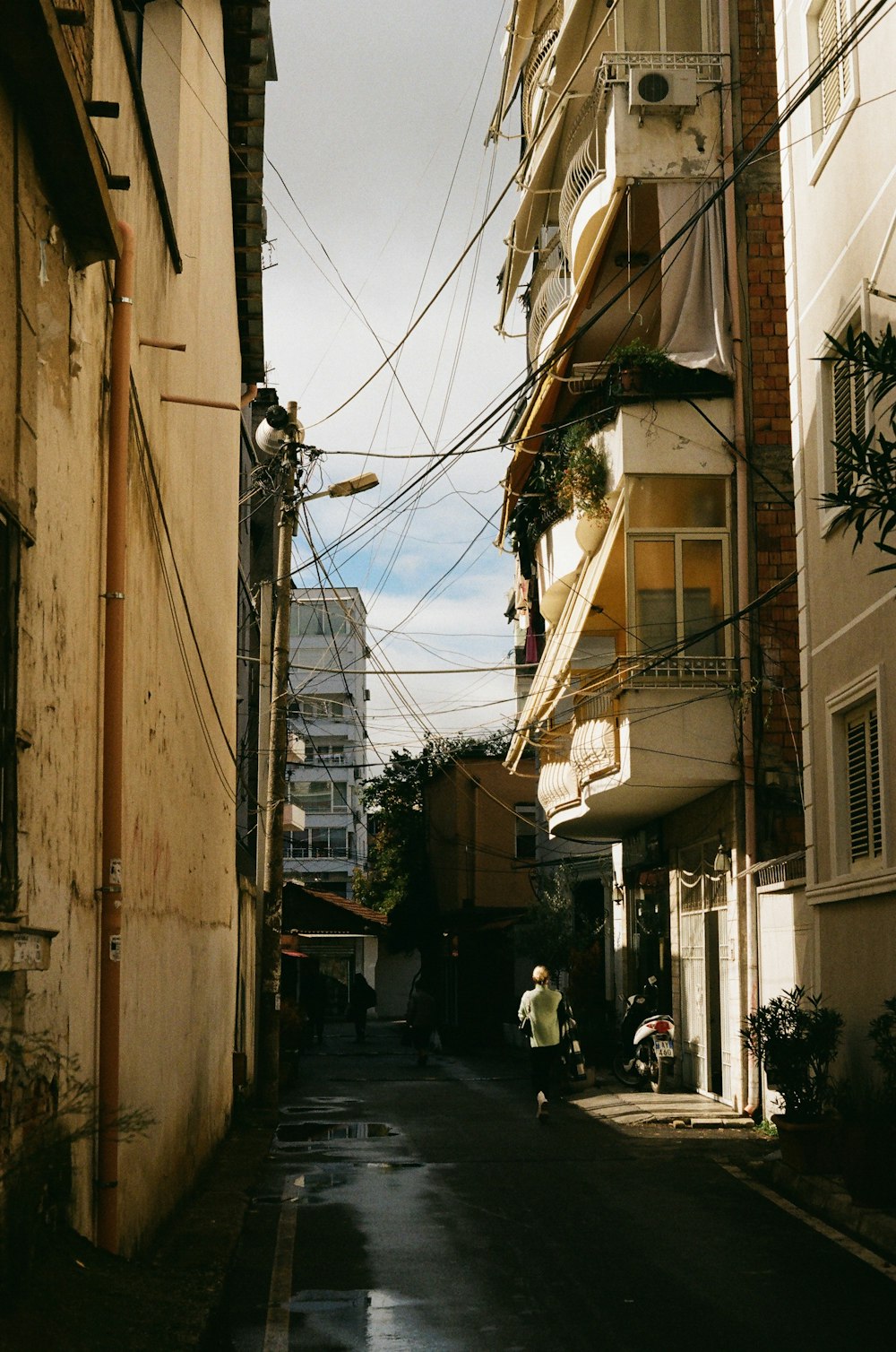 a narrow city street with a few people walking down it