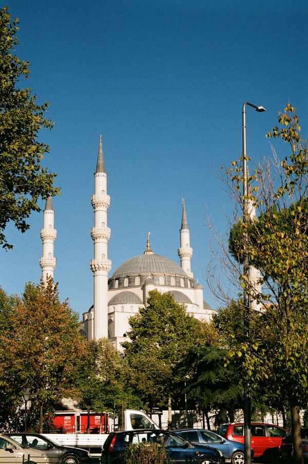 White mosque with a grand dome and four slender minarets rising above trees in Tirana