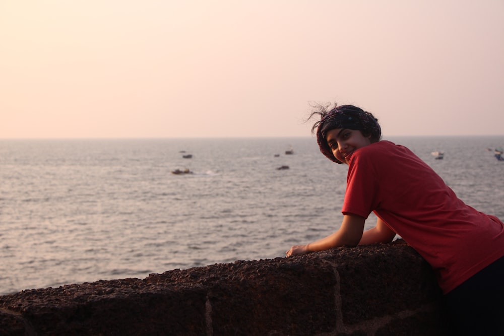 a woman leaning on a wall near the ocean