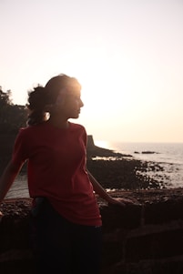a woman in a red shirt standing next to the ocean