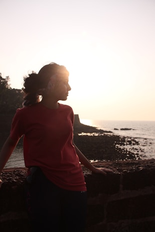 a woman in a red shirt standing next to the ocean