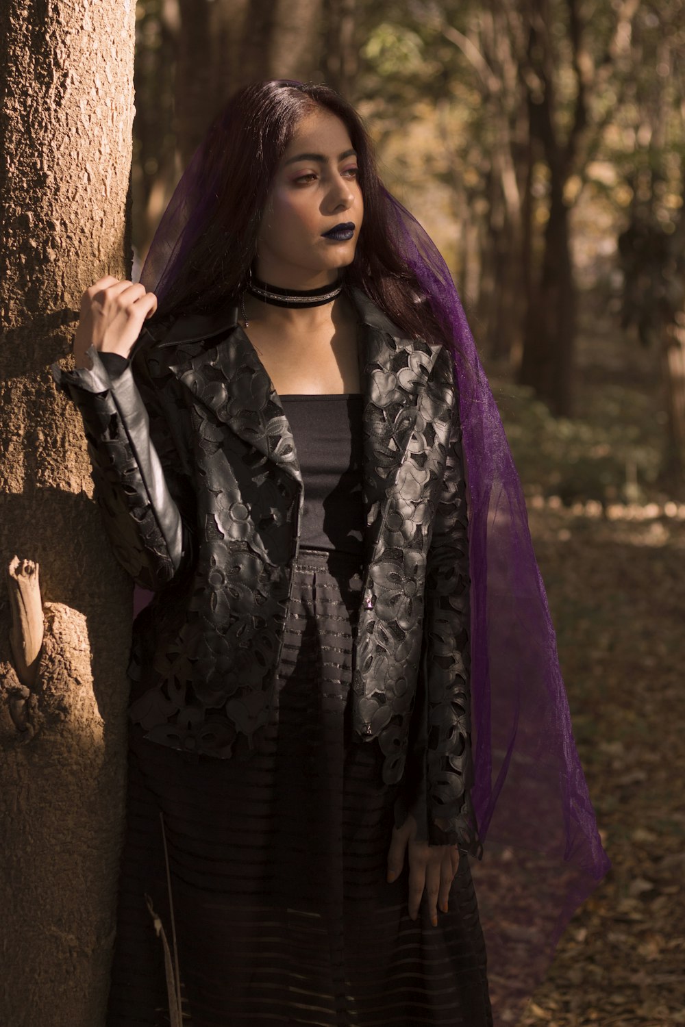 a woman with purple hair standing next to a tree