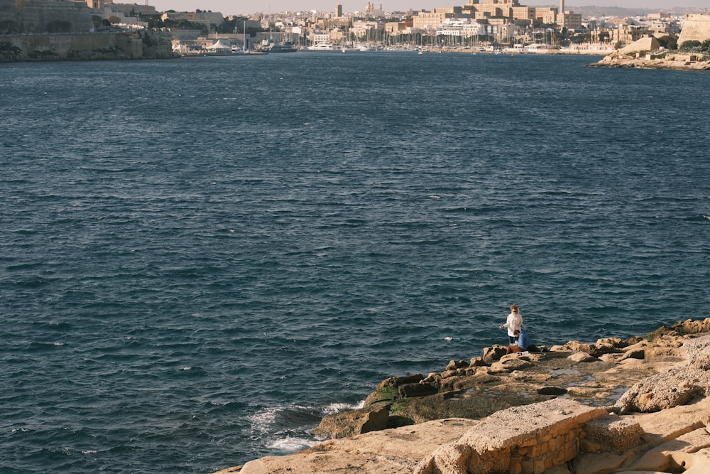 a man standing on the edge of a cliff next to a body of water