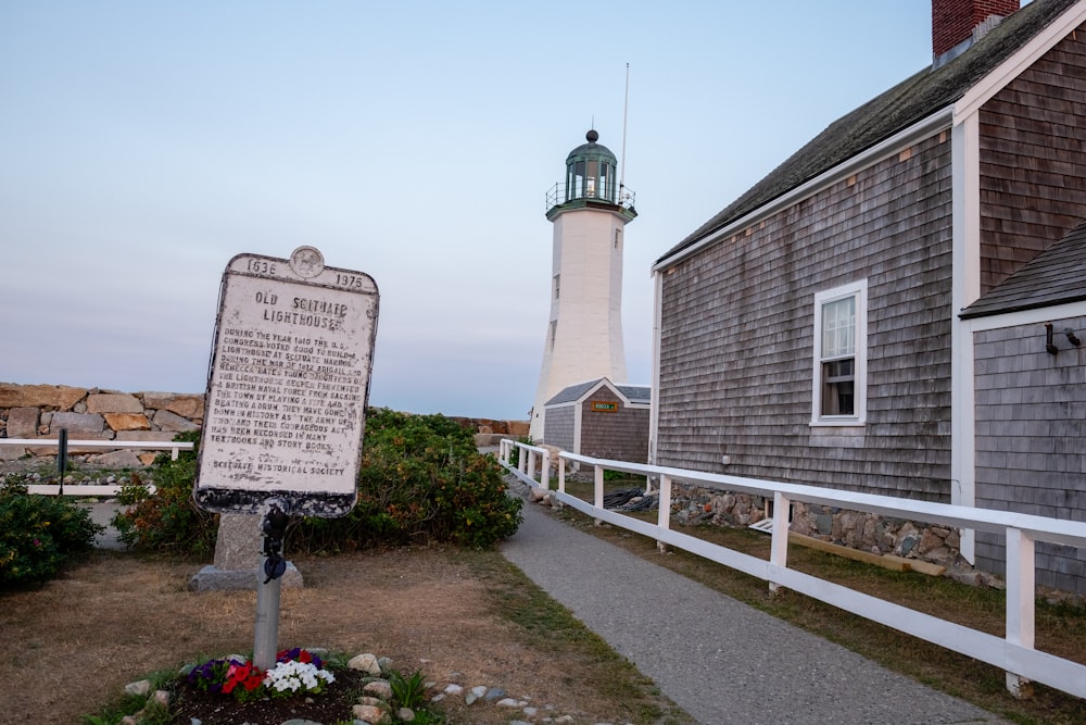 a sign in front of a house with a lighthouse in the background
