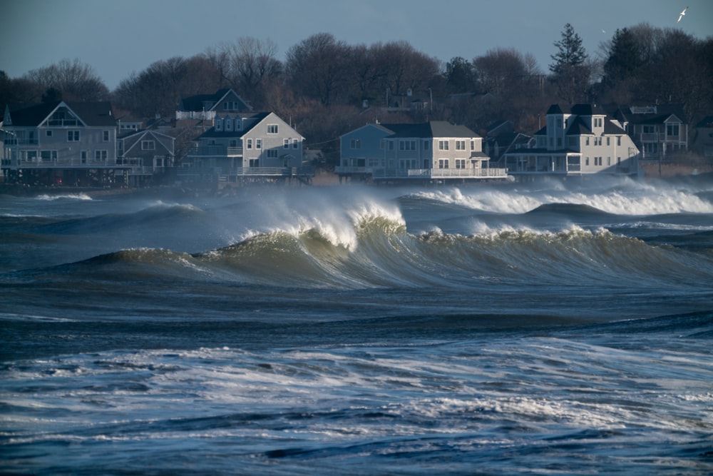 a large wave is crashing in front of a row of houses