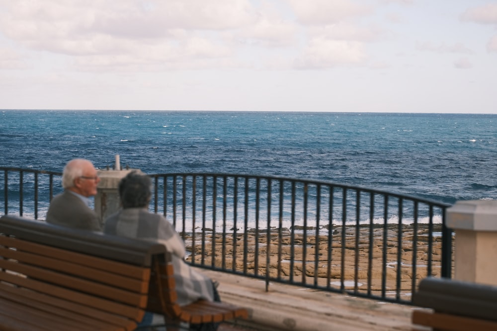 two people sitting on a bench looking out at the ocean