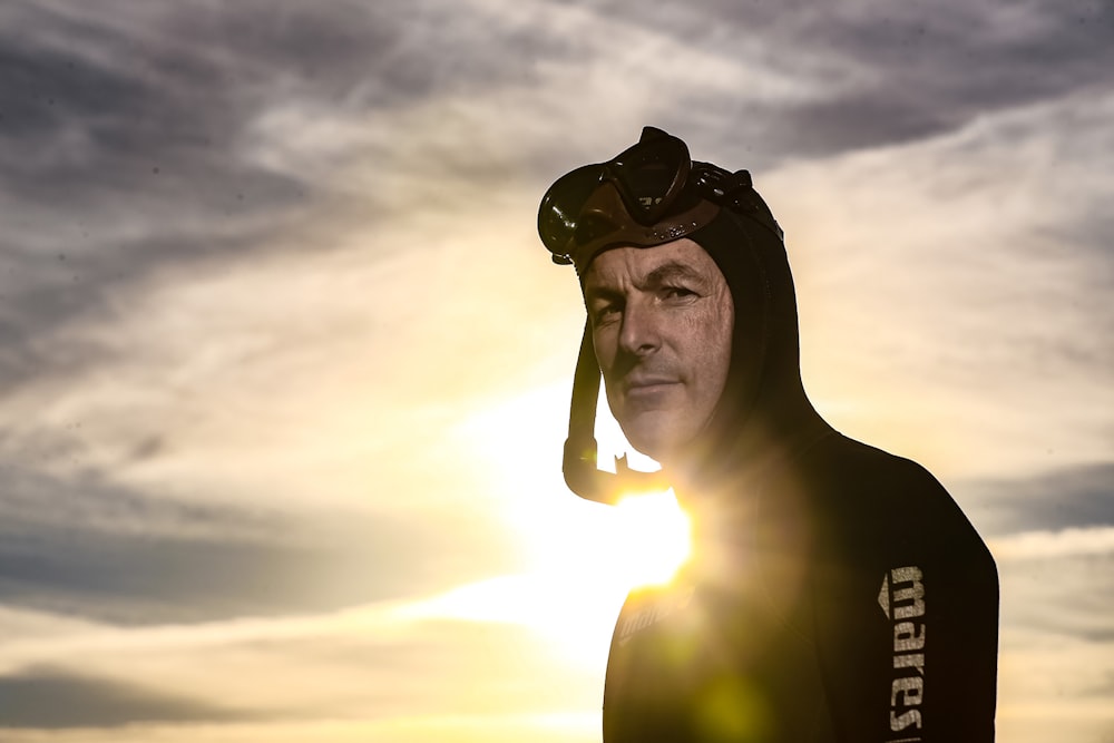 a man in a wet suit and goggles standing in front of the sun