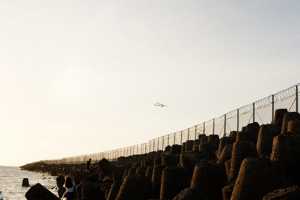 a plane is flying over the water near a fence
