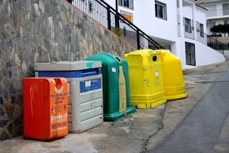 a row of brightly colored trash cans next to a stone wall