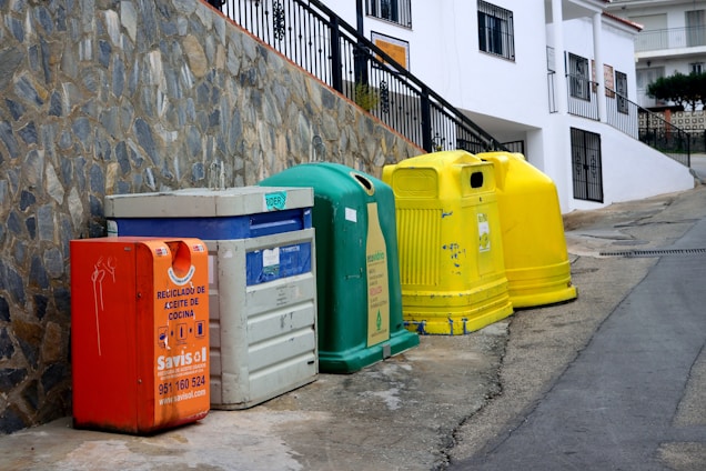 a row of brightly colored trash cans next to a stone wall