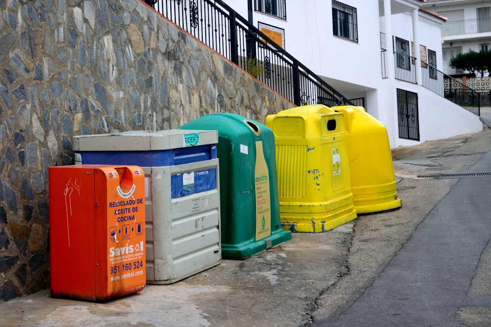 a row of brightly colored trash cans next to a stone wall