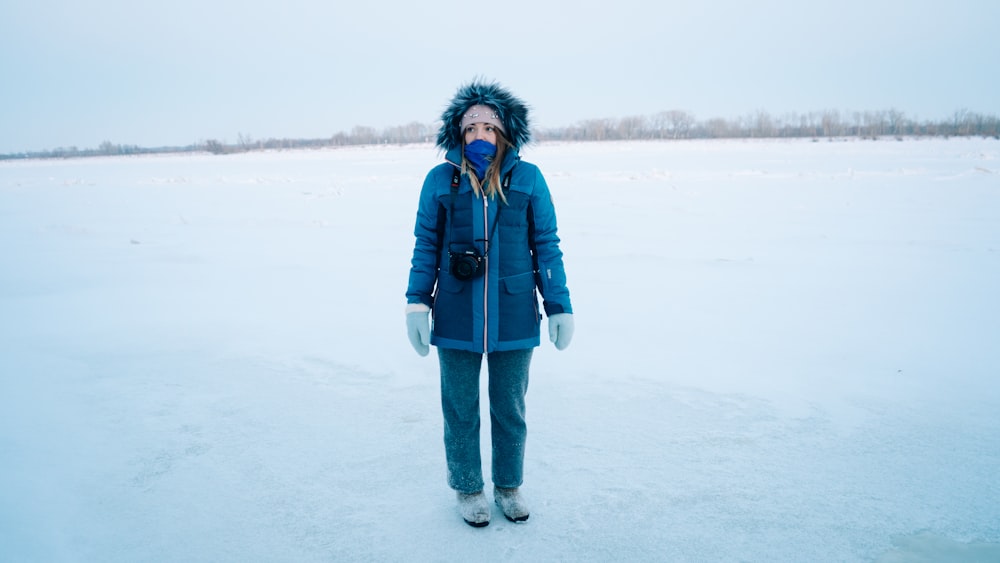 a woman standing in the snow wearing a blue jacket
