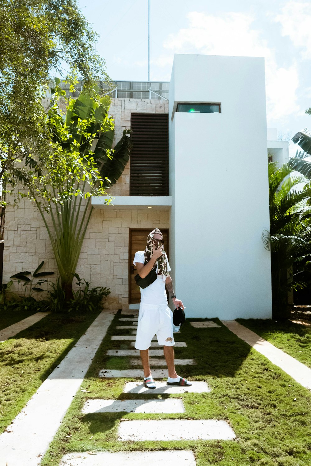 a man in a white shirt and white shorts standing in front of a house