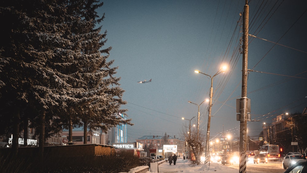a snowy street at night with a plane flying overhead