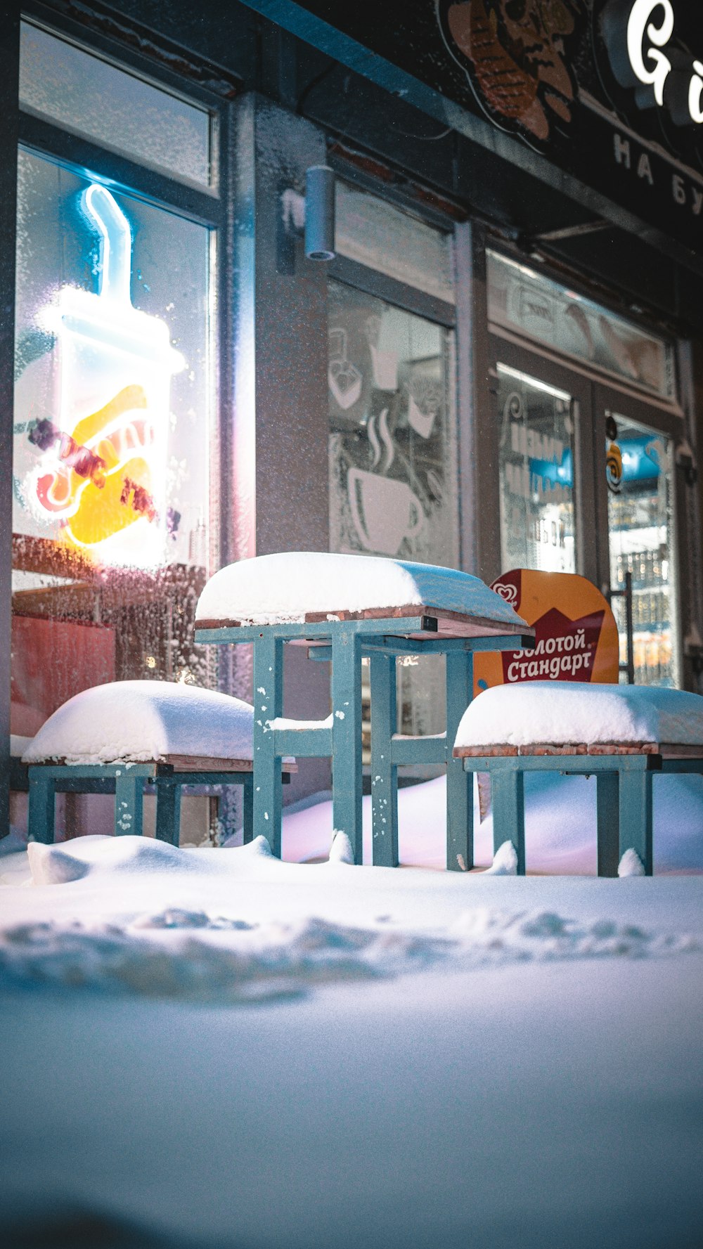 a couple of benches covered in snow in front of a store