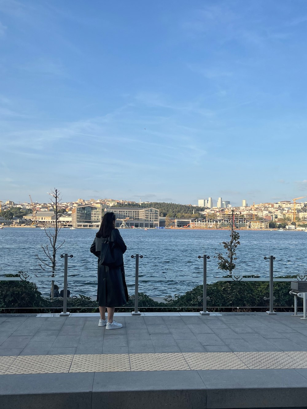 a woman standing on a sidewalk next to a body of water