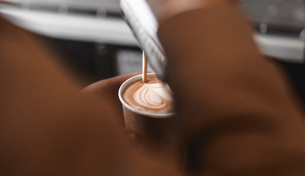 a person holding a cup of coffee with a toothbrush in it