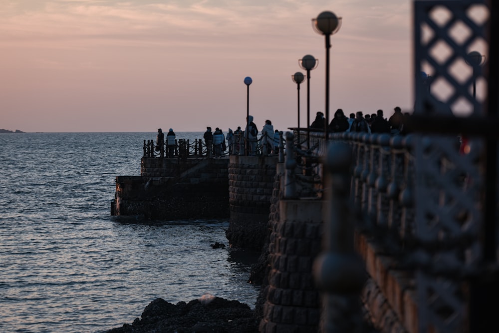 a group of people standing on a pier next to the ocean