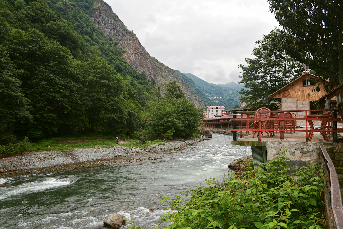 A rocky river beside a cafe terrace at Ayder, under steep forested slopes