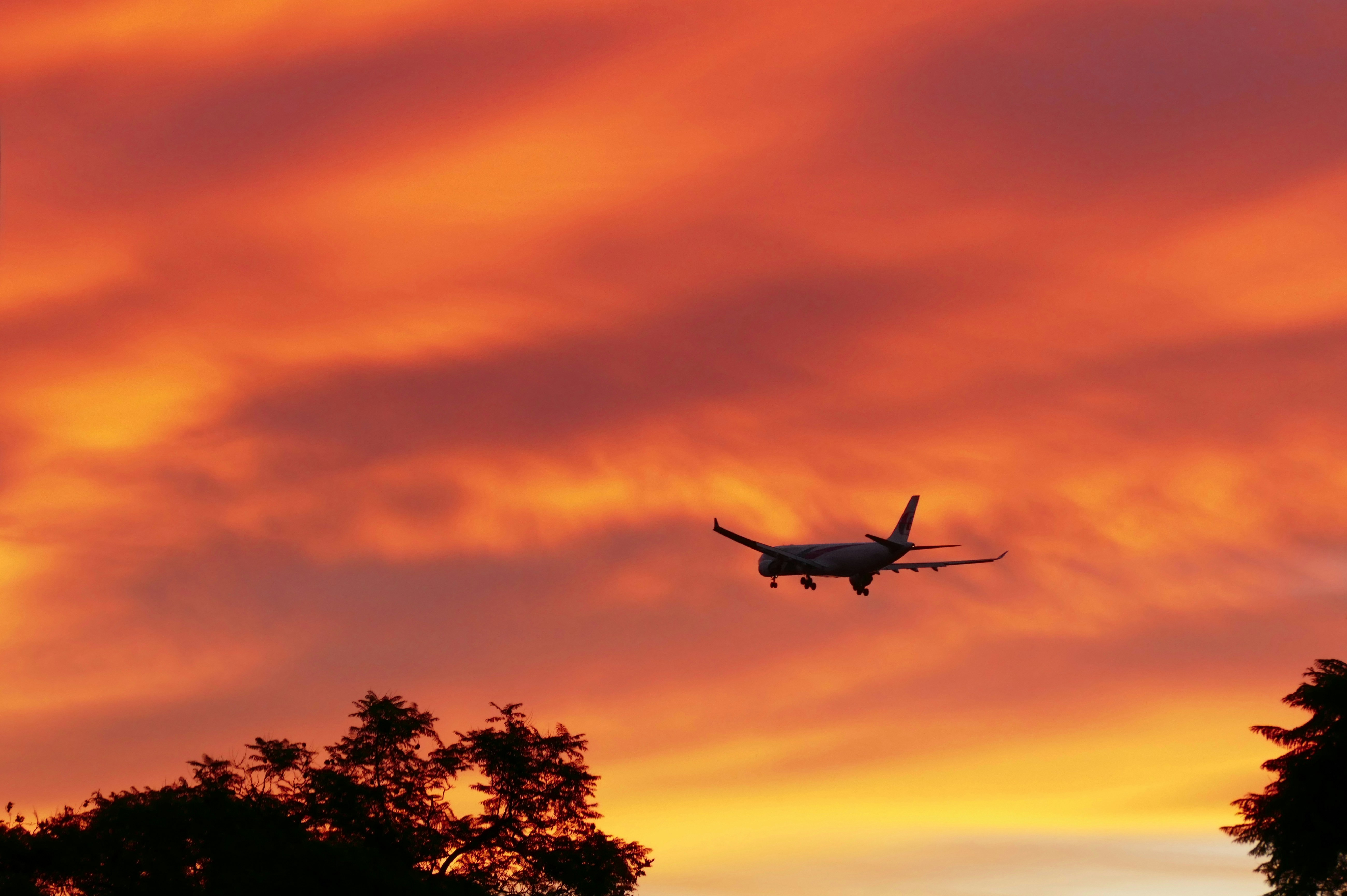 a plane is flying in the sky at sunset, Airplane Silhouette Against Dramatic Sunset Sky