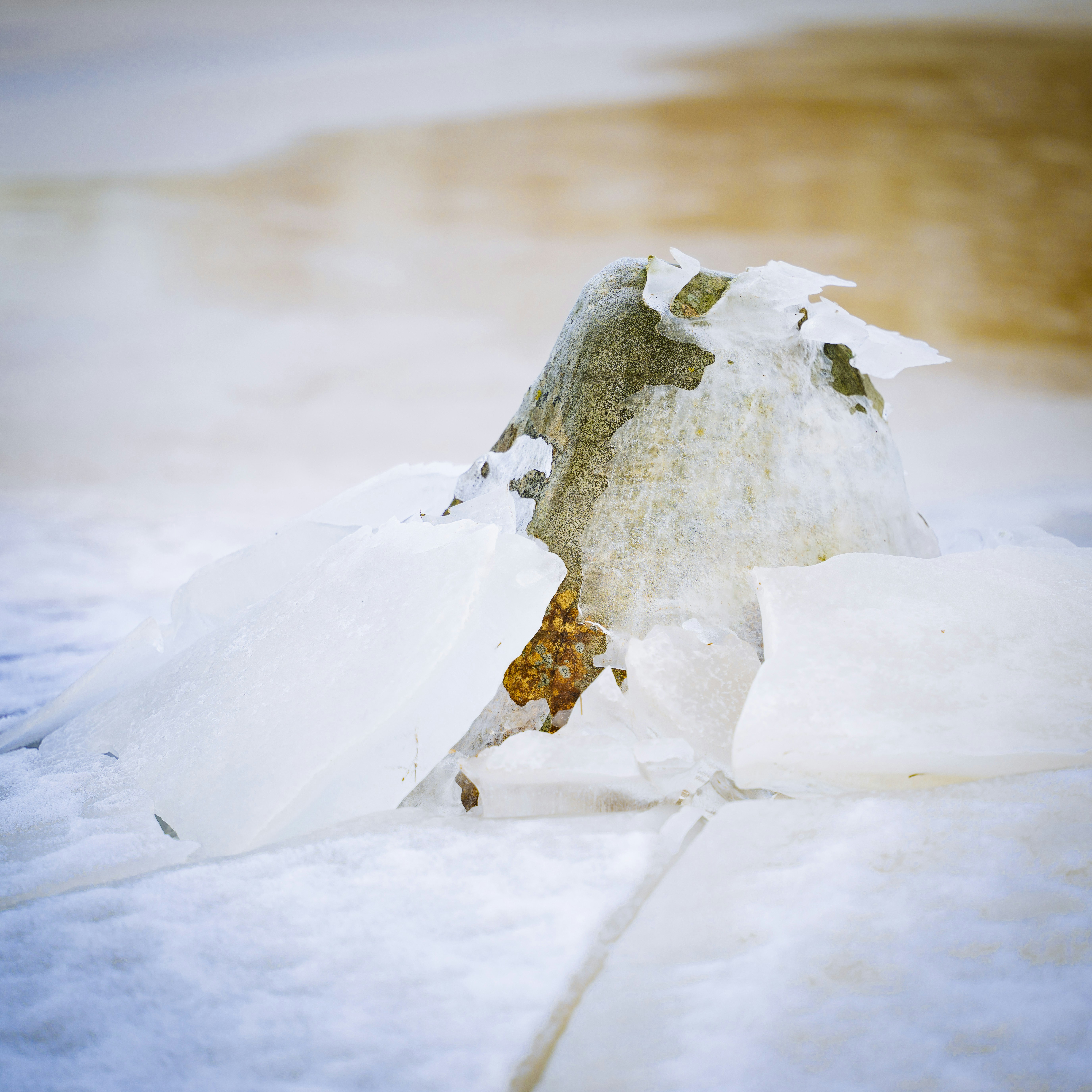 a rock covered in snow next to a body of water