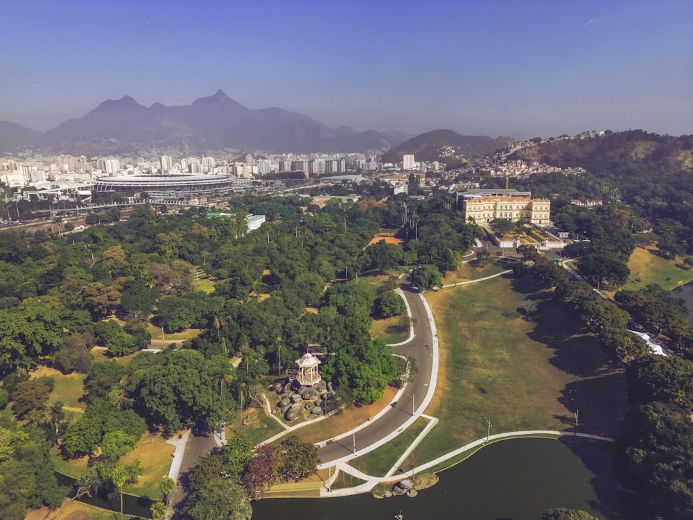 an aerial view of a park with a lake and mountains in the background